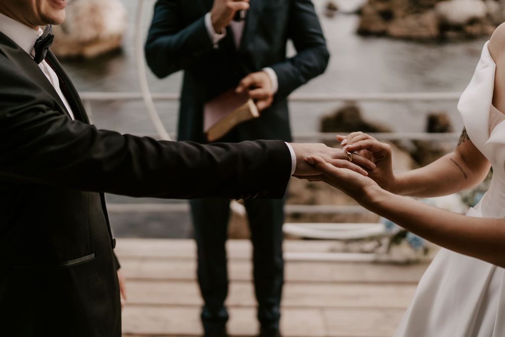 Close-up of hands during a ring exchange ceremony at an outdoor waterfront wedding.