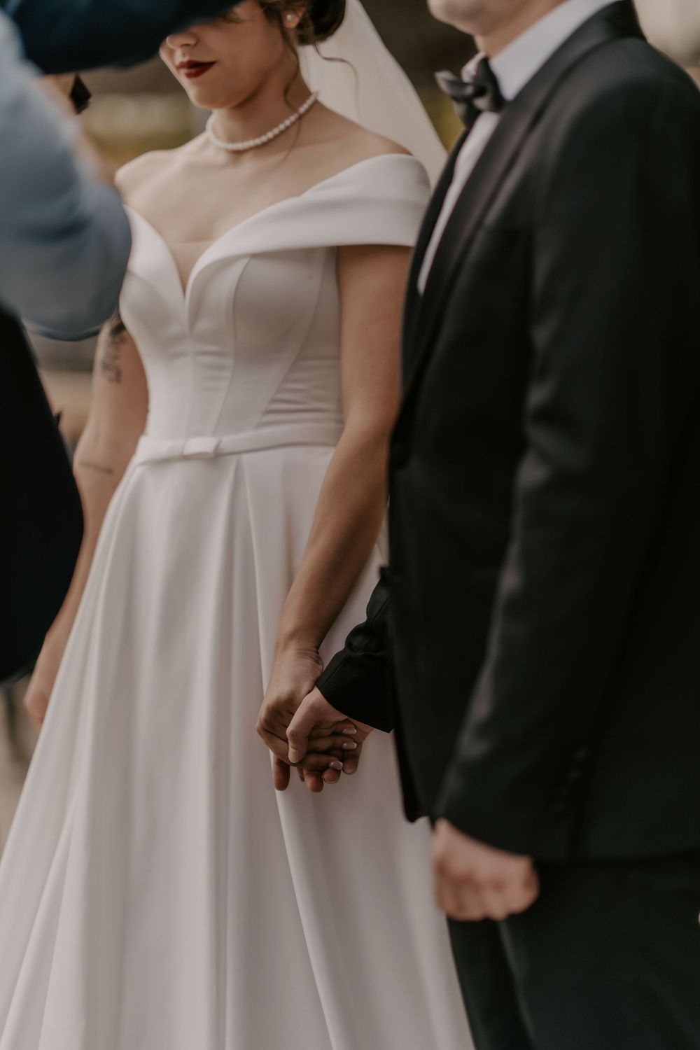 Detail shot of an elegant off-shoulder white wedding gown and formal attire during the ceremony.