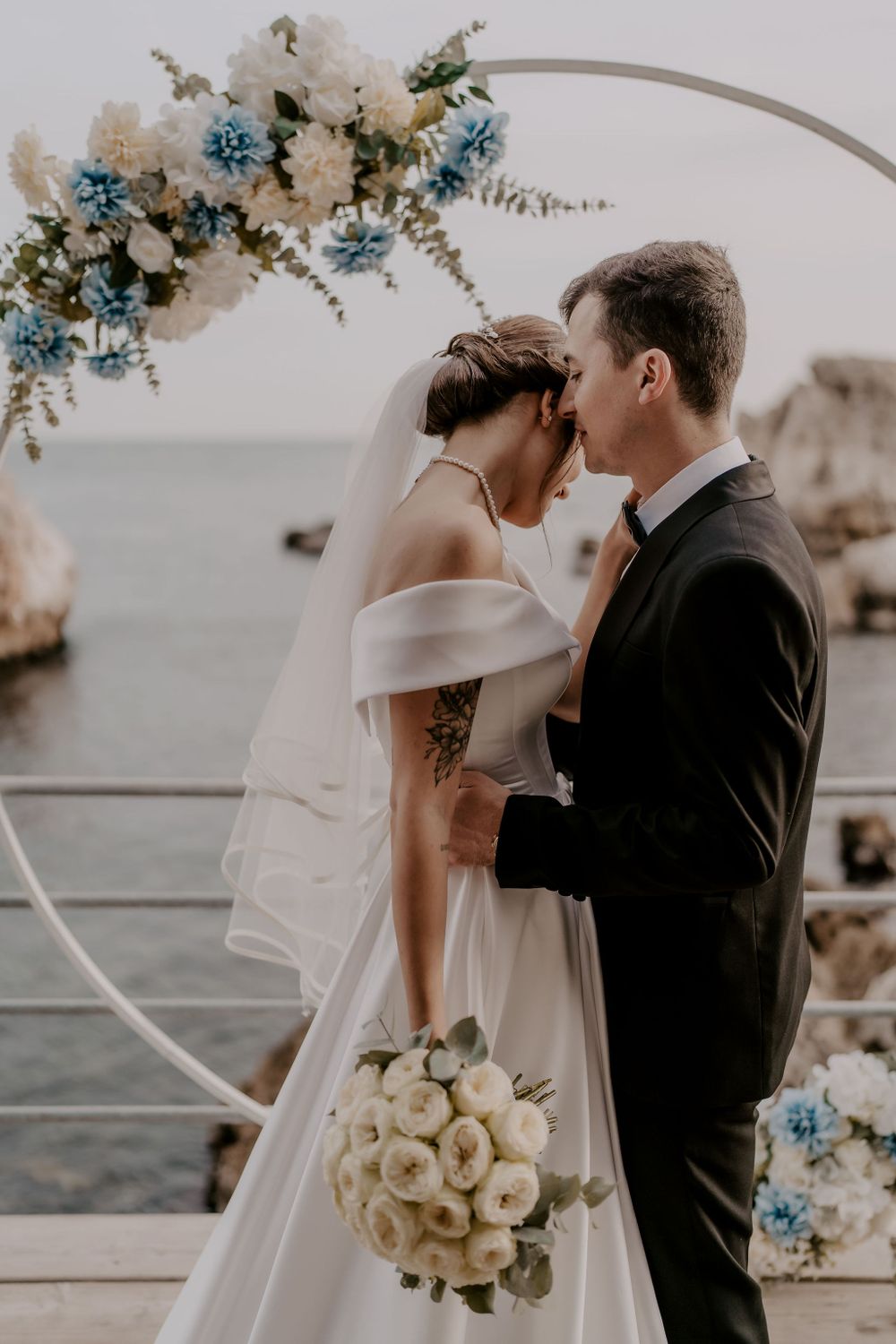 A romantic wedding ceremony on a seaside deck with white and blue floral arch decorations and ocean views.
