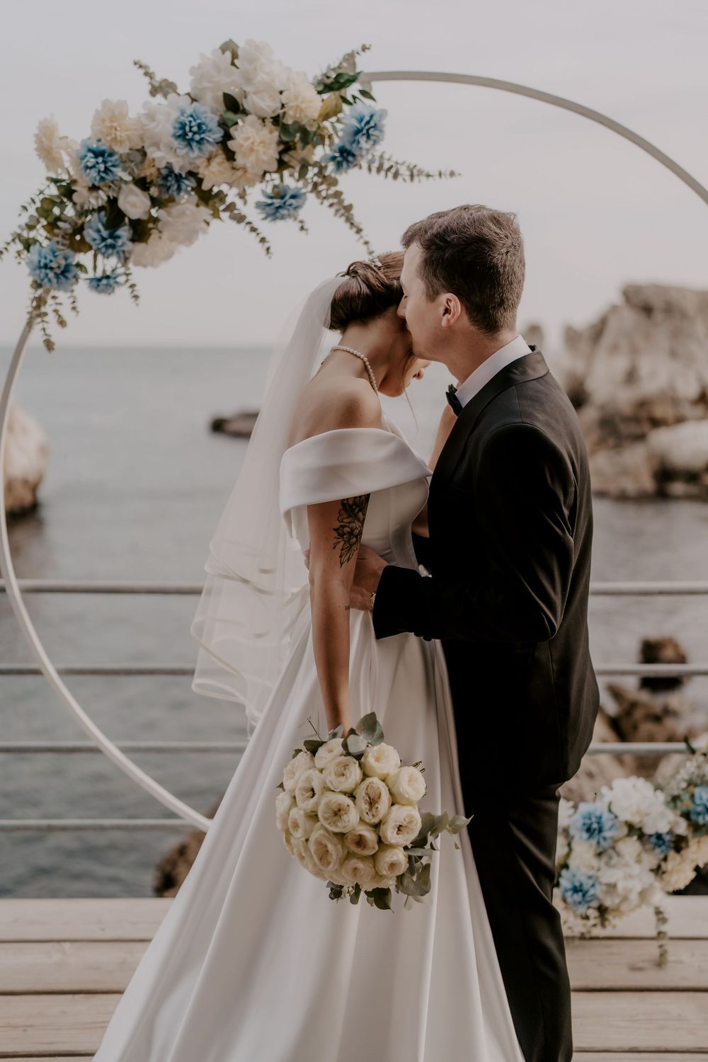Intimate waterfront wedding moment with elegant white bouquet and coastal backdrop.