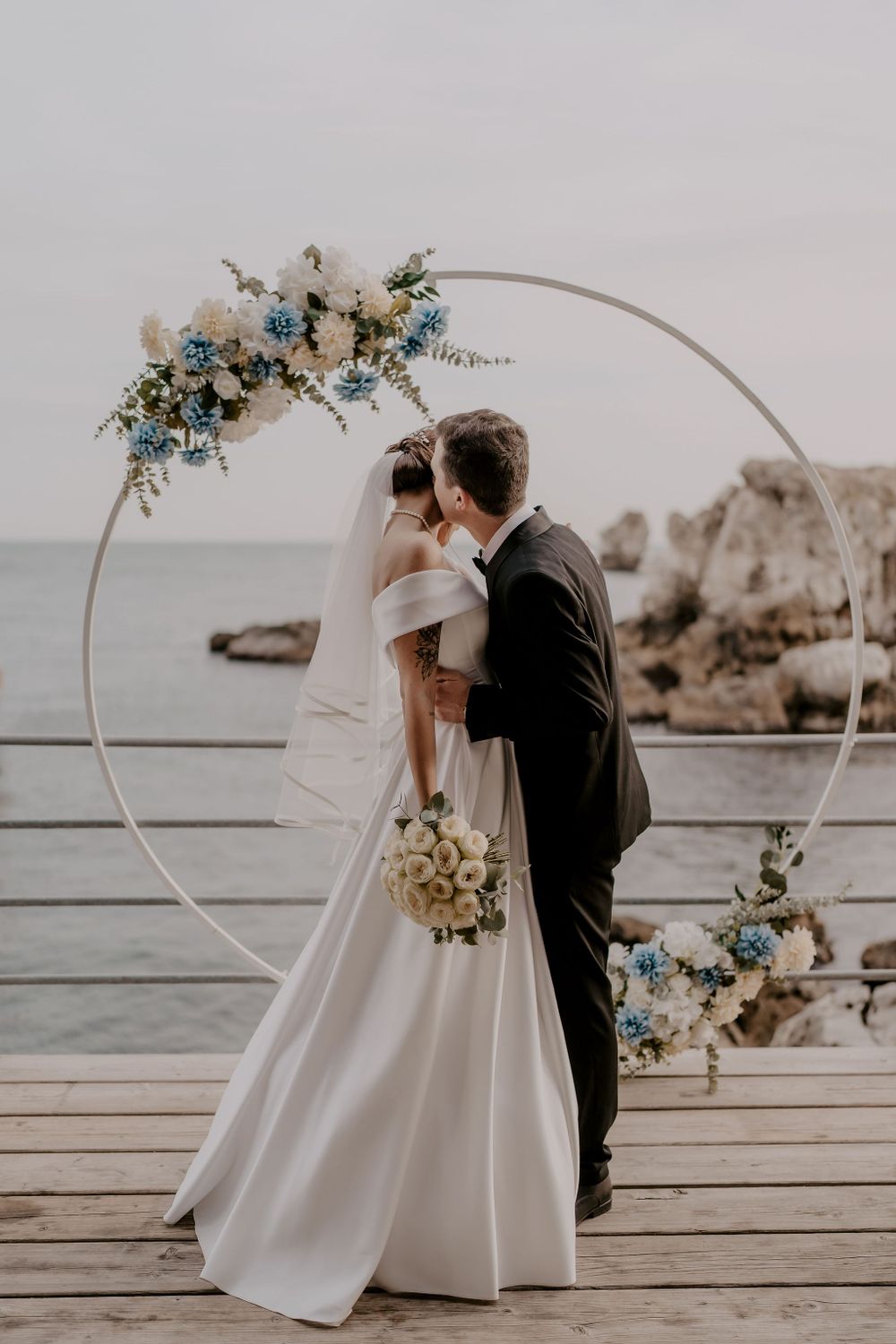 Seaside wedding ceremony with minimalist decor featuring white and blue florals against ocean scenery.