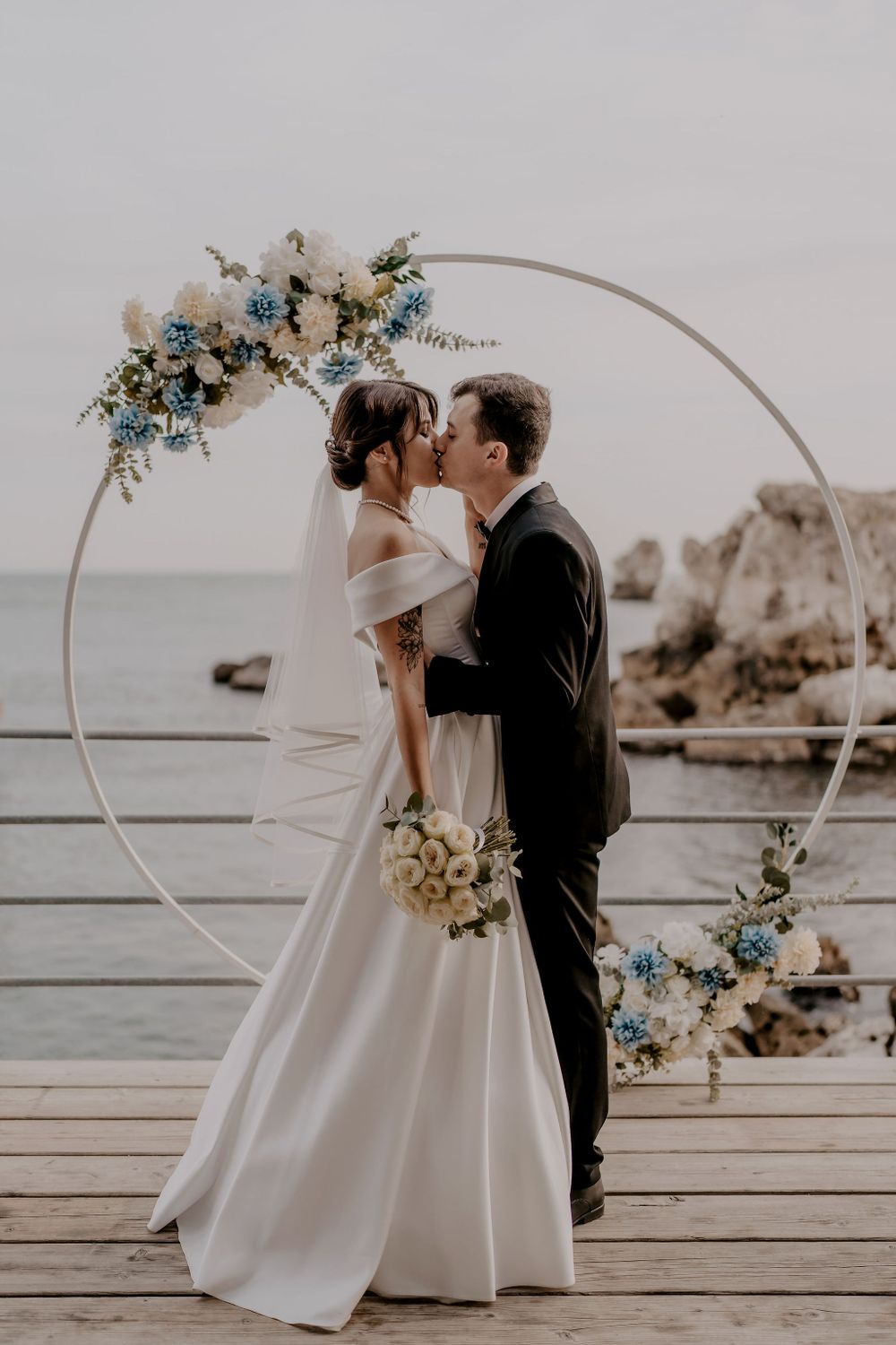 Elegant oceanfront wedding ceremony with circular arch and white floral arrangements.