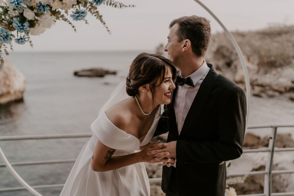 Romantic coastal wedding moment captured under decorated arch with ocean views.