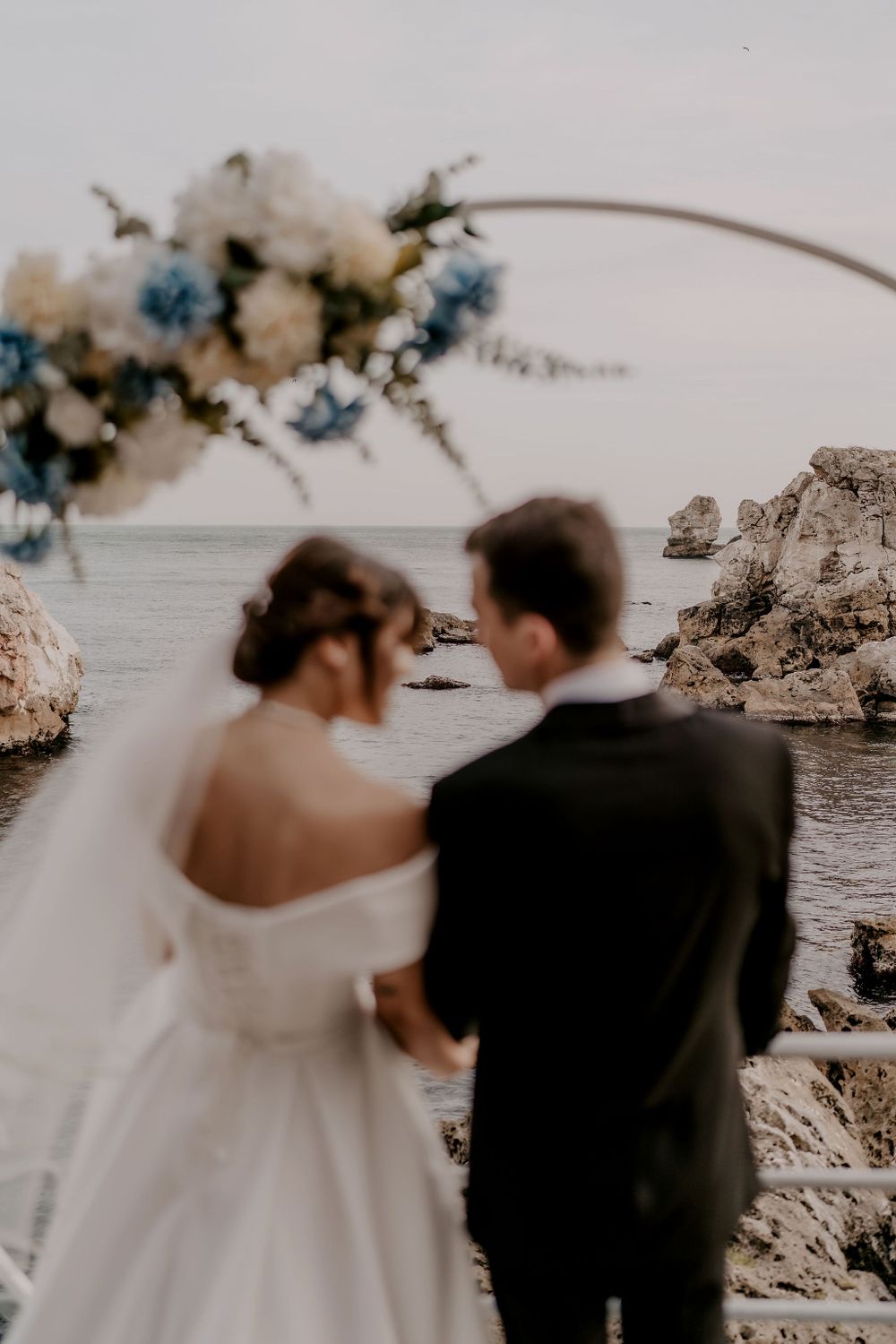 Dreamy waterfront wedding scene with floral arch and rocky coastal backdrop.