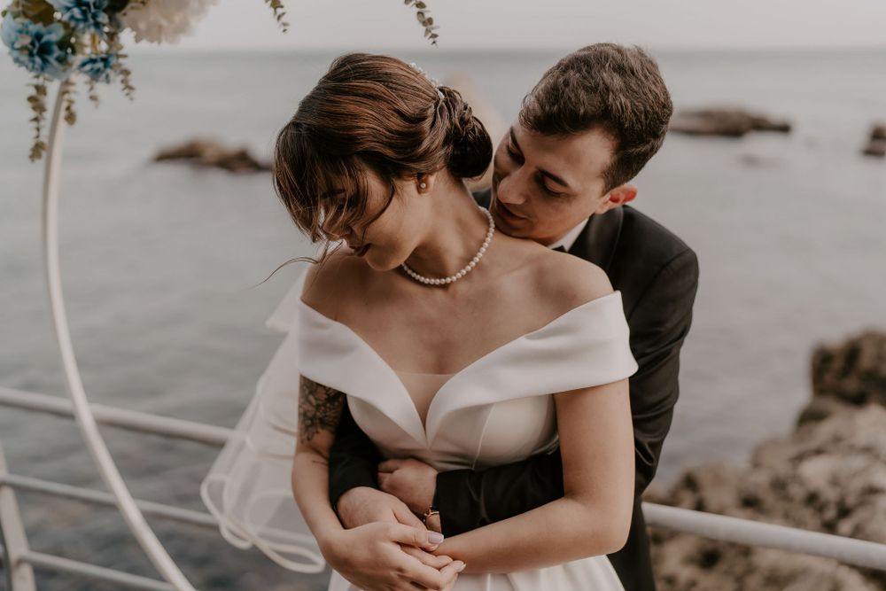 Tender moment between newlyweds during seaside ceremony with floral decorations.