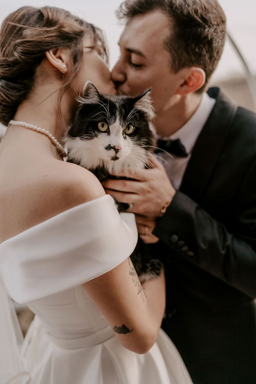 Newlyweds share a tender moment while holding their black and white cat during wedding photos.