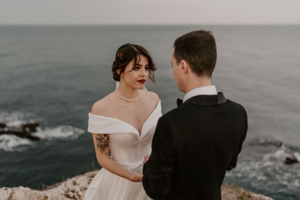 Newlyweds share an intimate moment on a coastal cliff with the sea as their backdrop.