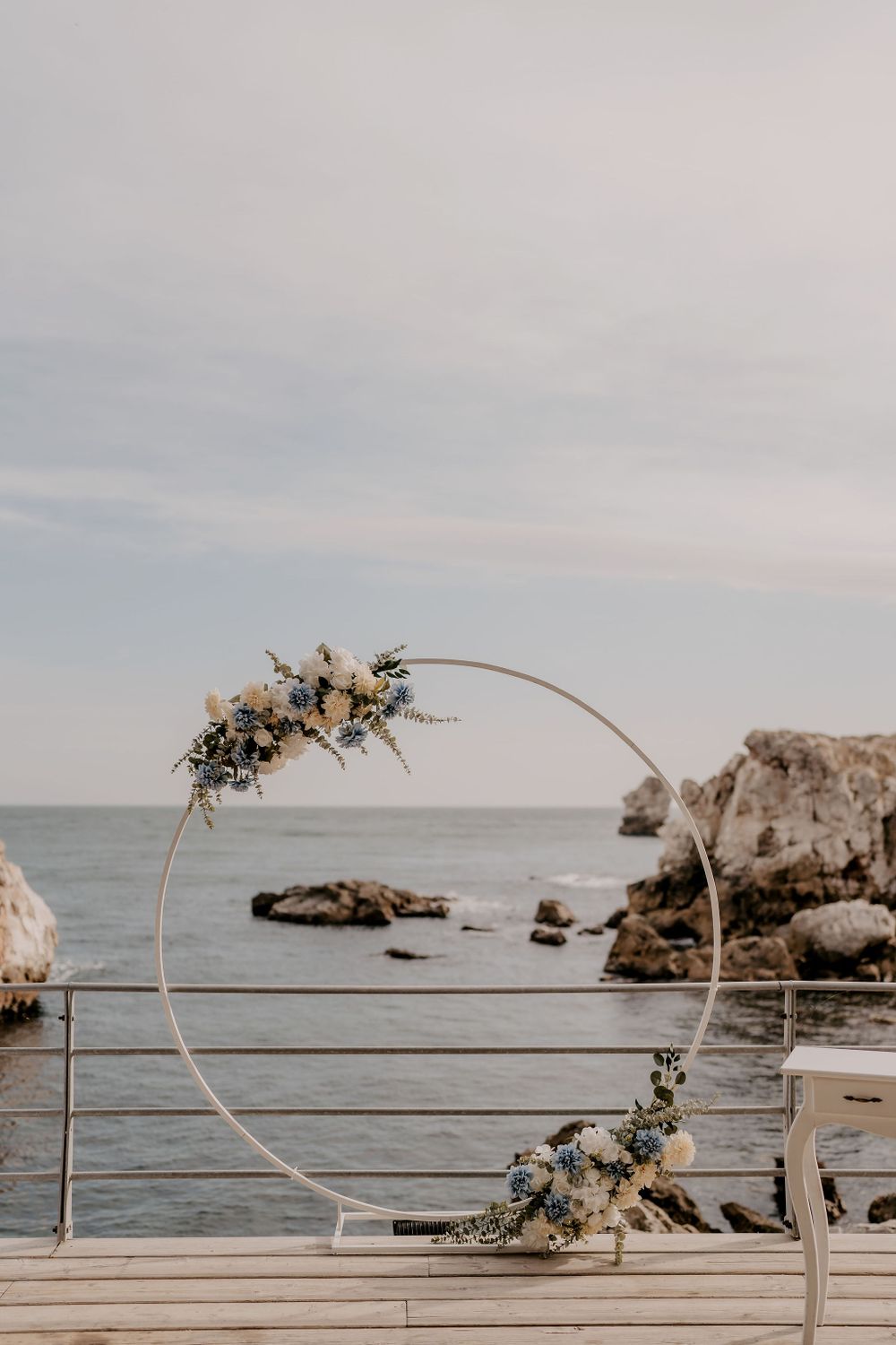 Seaside wedding ceremony arch with floral arrangements overlooking rocky ocean coastline.