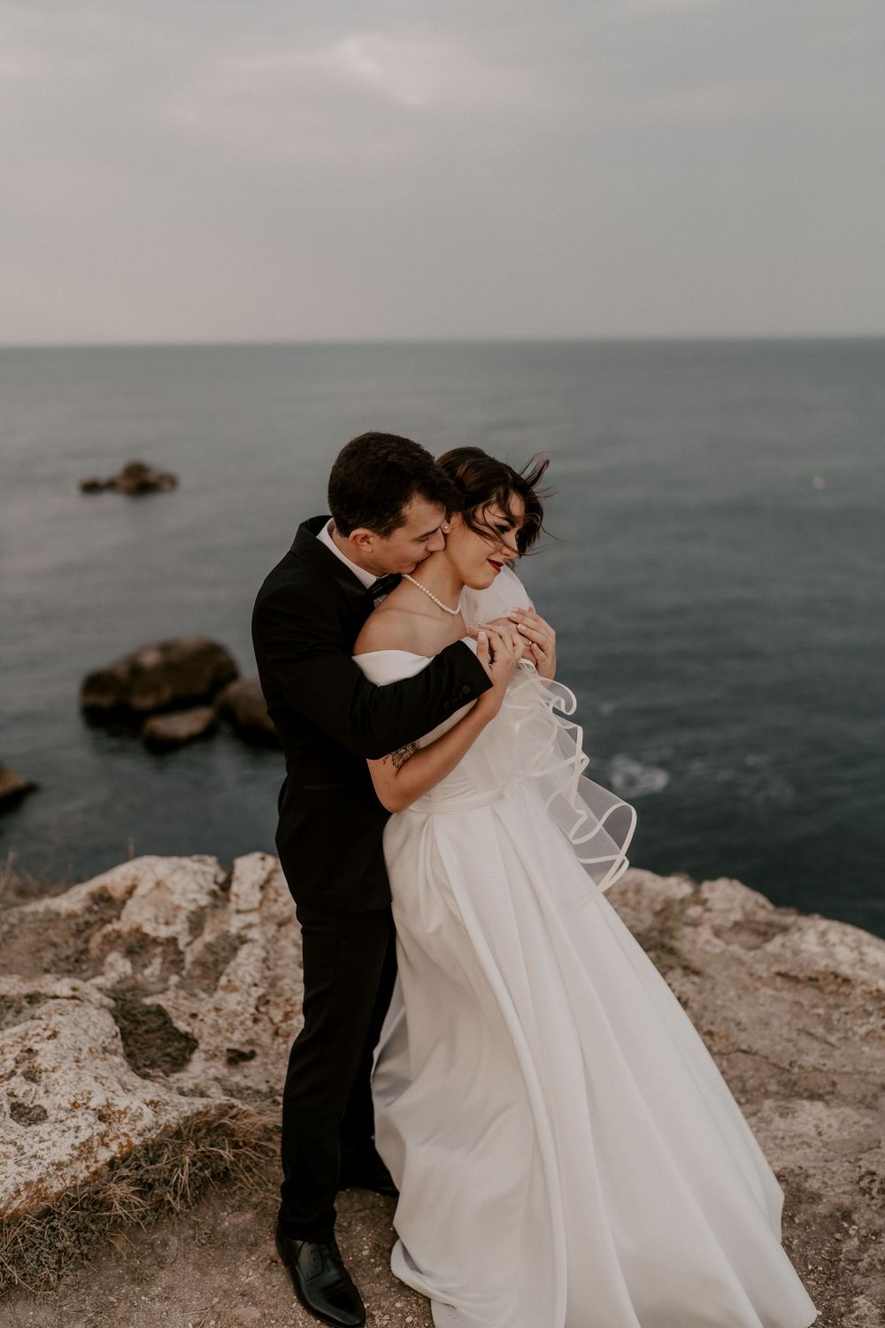 Romantic wedding embrace on a dramatic oceanside cliff during golden hour.