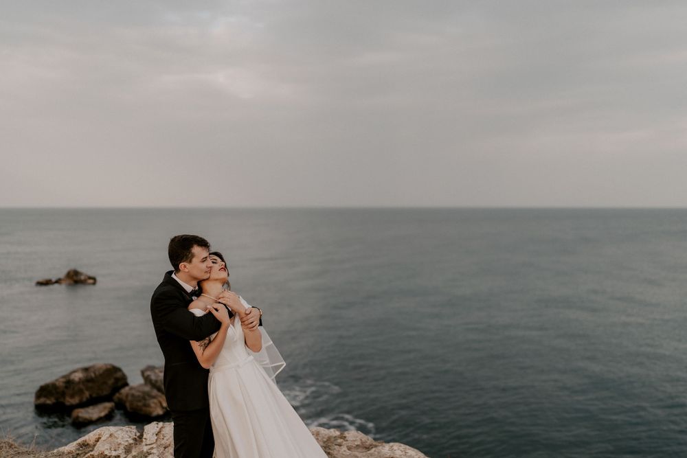Joyful wedding embrace captured on dramatic coastal cliffs overlooking the ocean.