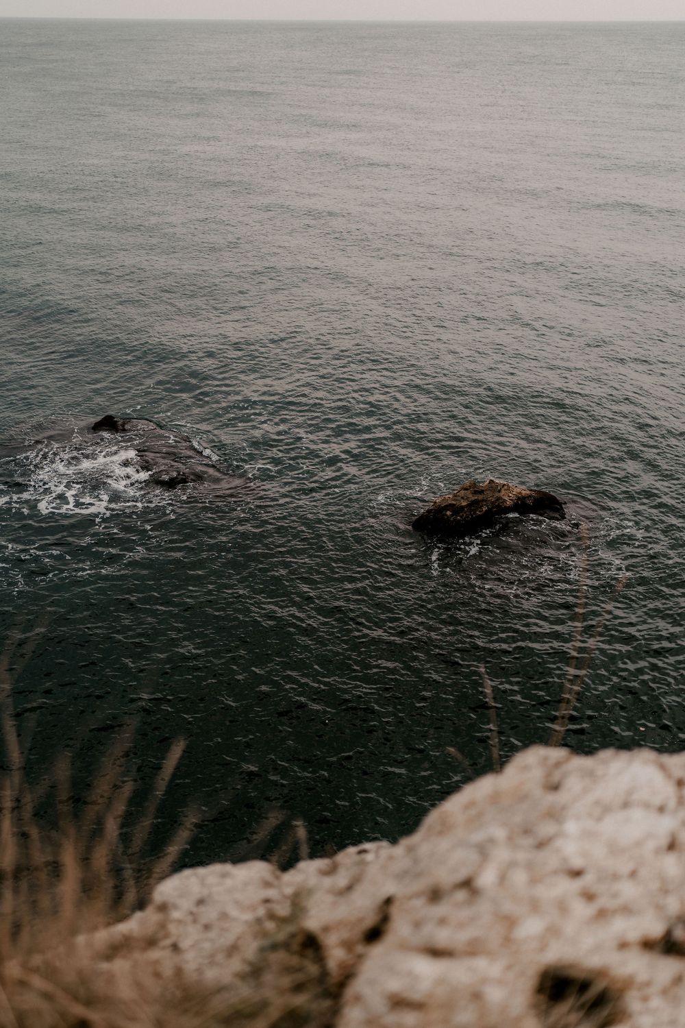 Rocky coastal landscape with waves crashing against offshore rocks viewed from cliff edge.