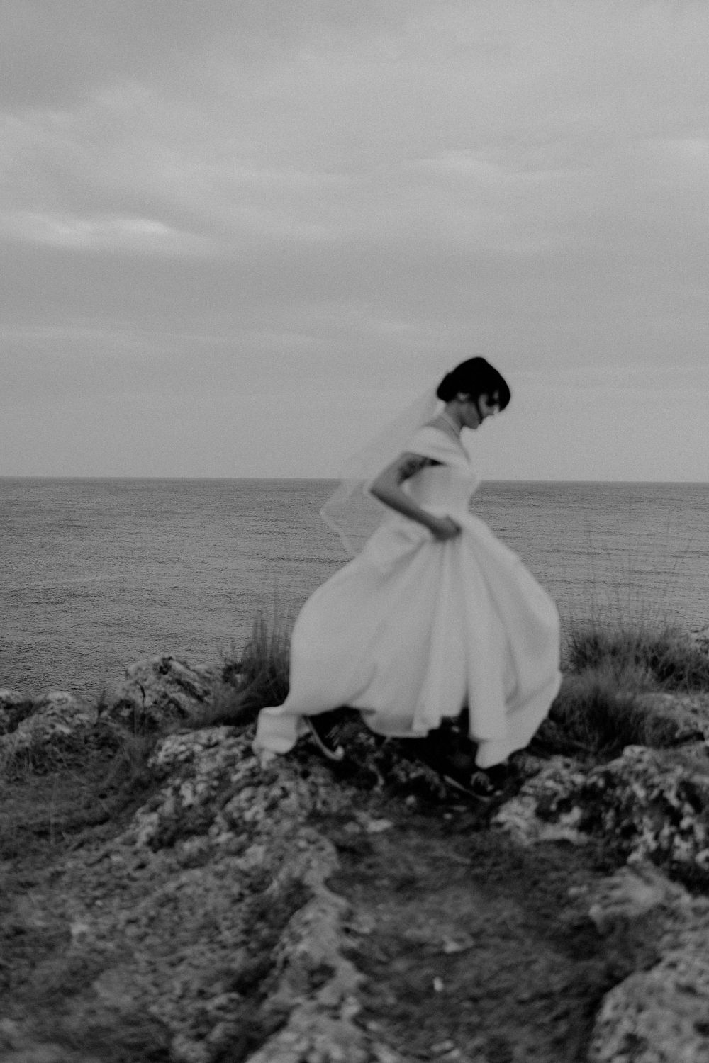 A couple in wedding attire explores rocky coastal cliffs with dramatic ocean views.