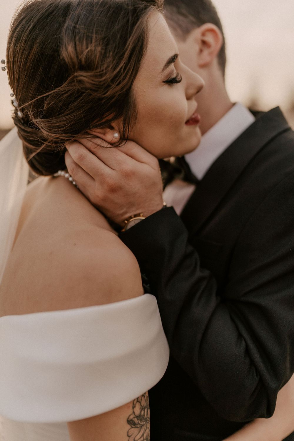 Intimate wedding moment captured in warm tones as couple embraces with bride in off-shoulder dress.