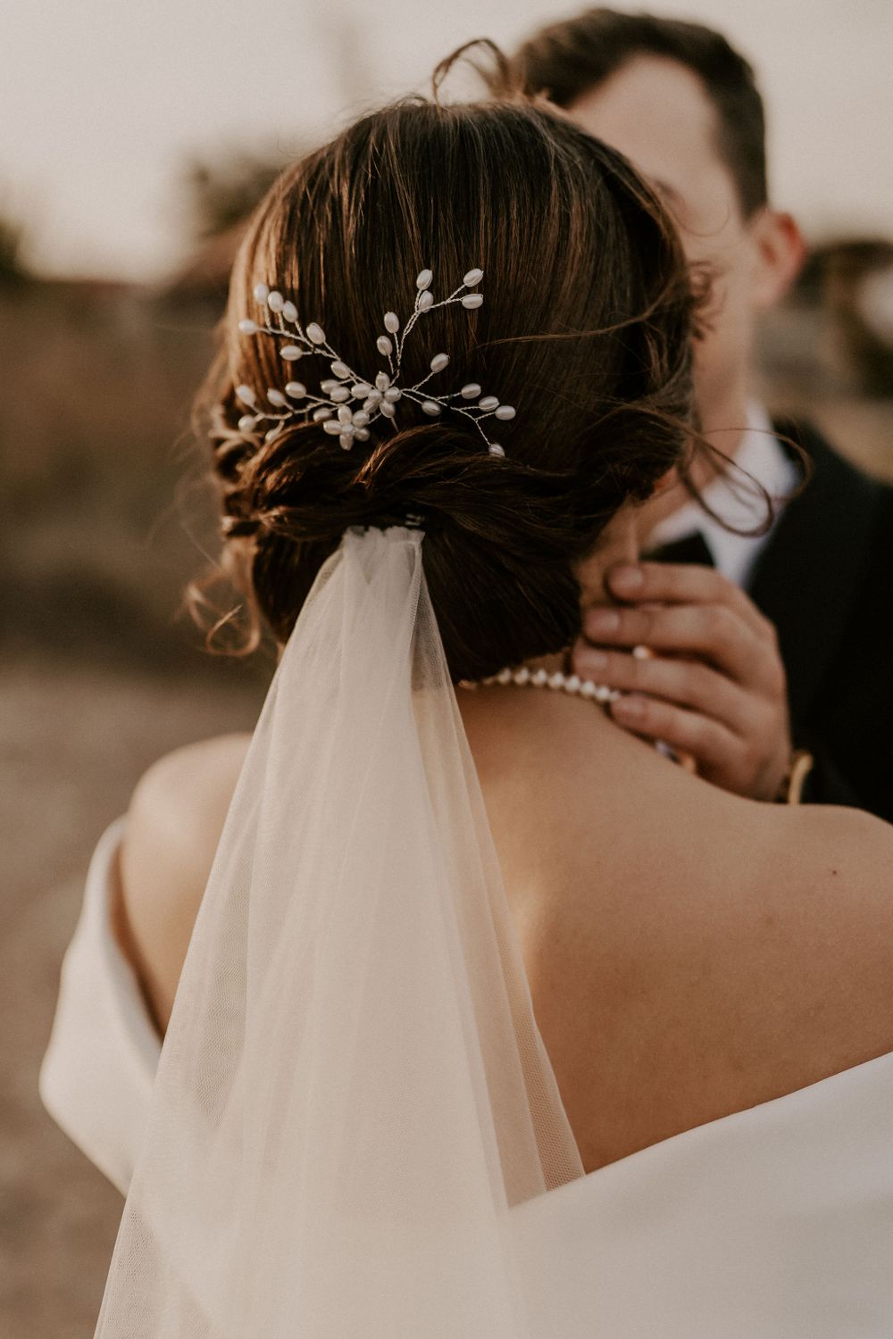 Elegant bridal hairstyle with pearl hair accessories and flowing veil against romantic backdrop.