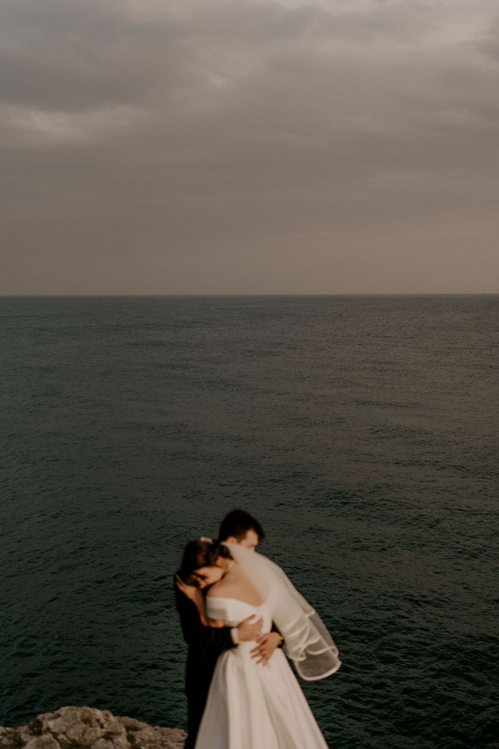 Intimate embrace on coastal cliff edge with moody ocean backdrop.