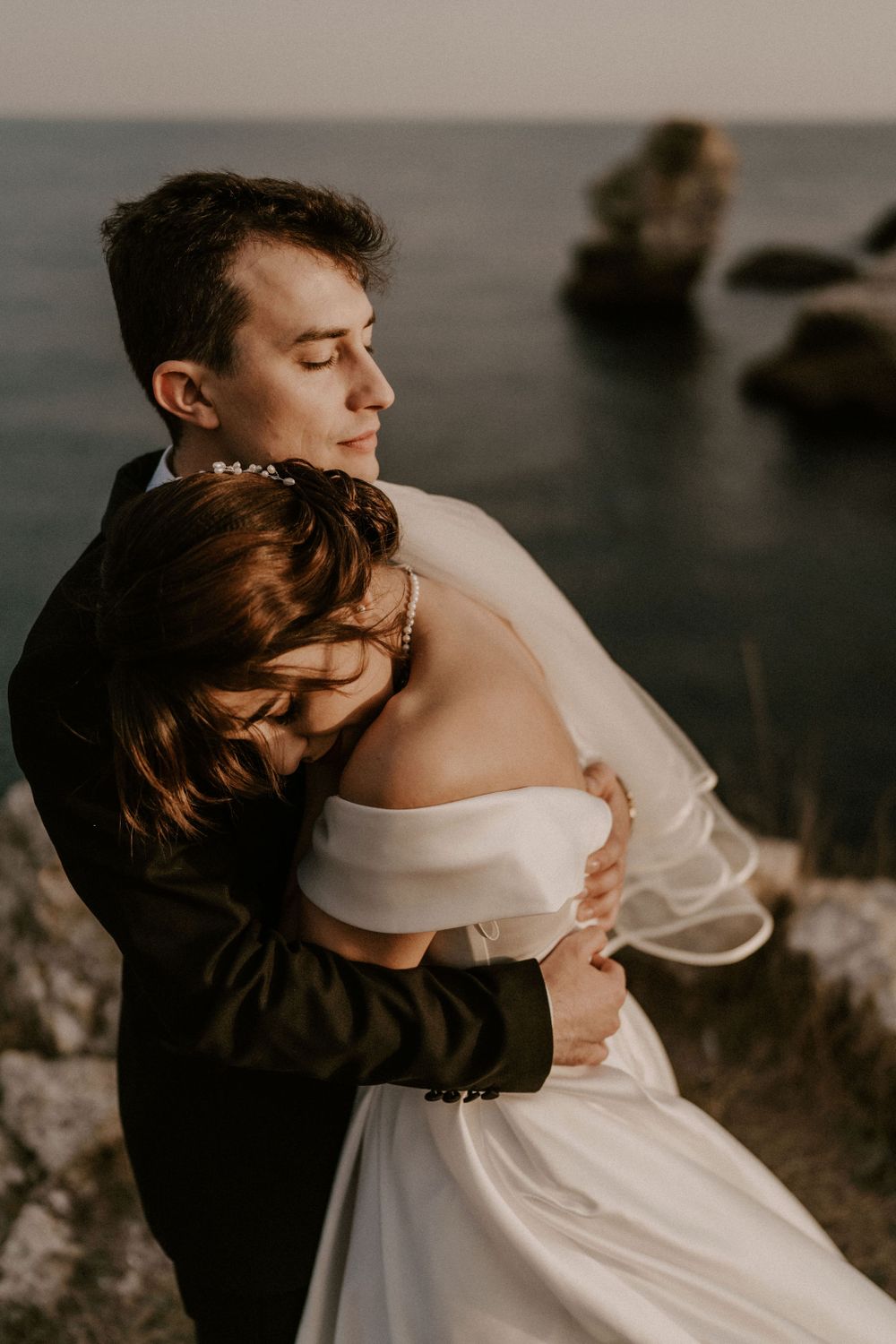Tender embrace against moody ocean backdrop during coastal wedding shoot.