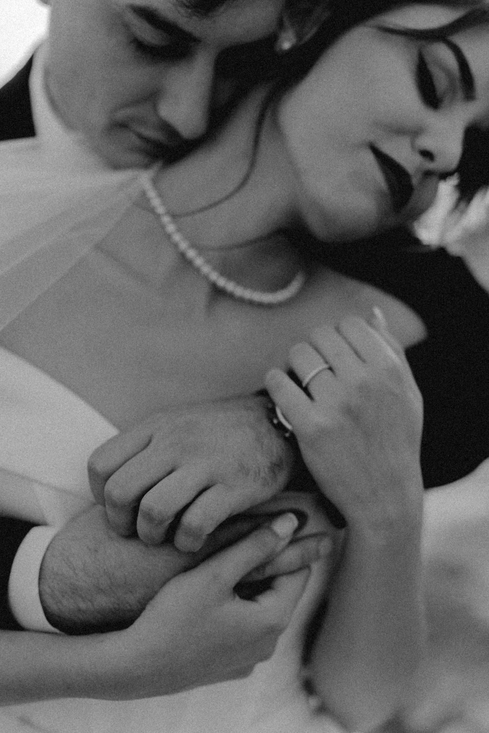 Black and white close-up of wedding rings and pearl necklace during intimate moment.