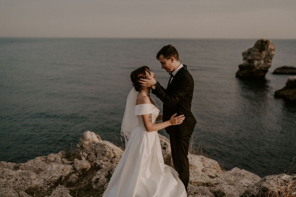 A couple shares an intimate moment on rugged coastal cliffs overlooking a vast ocean at sunset.