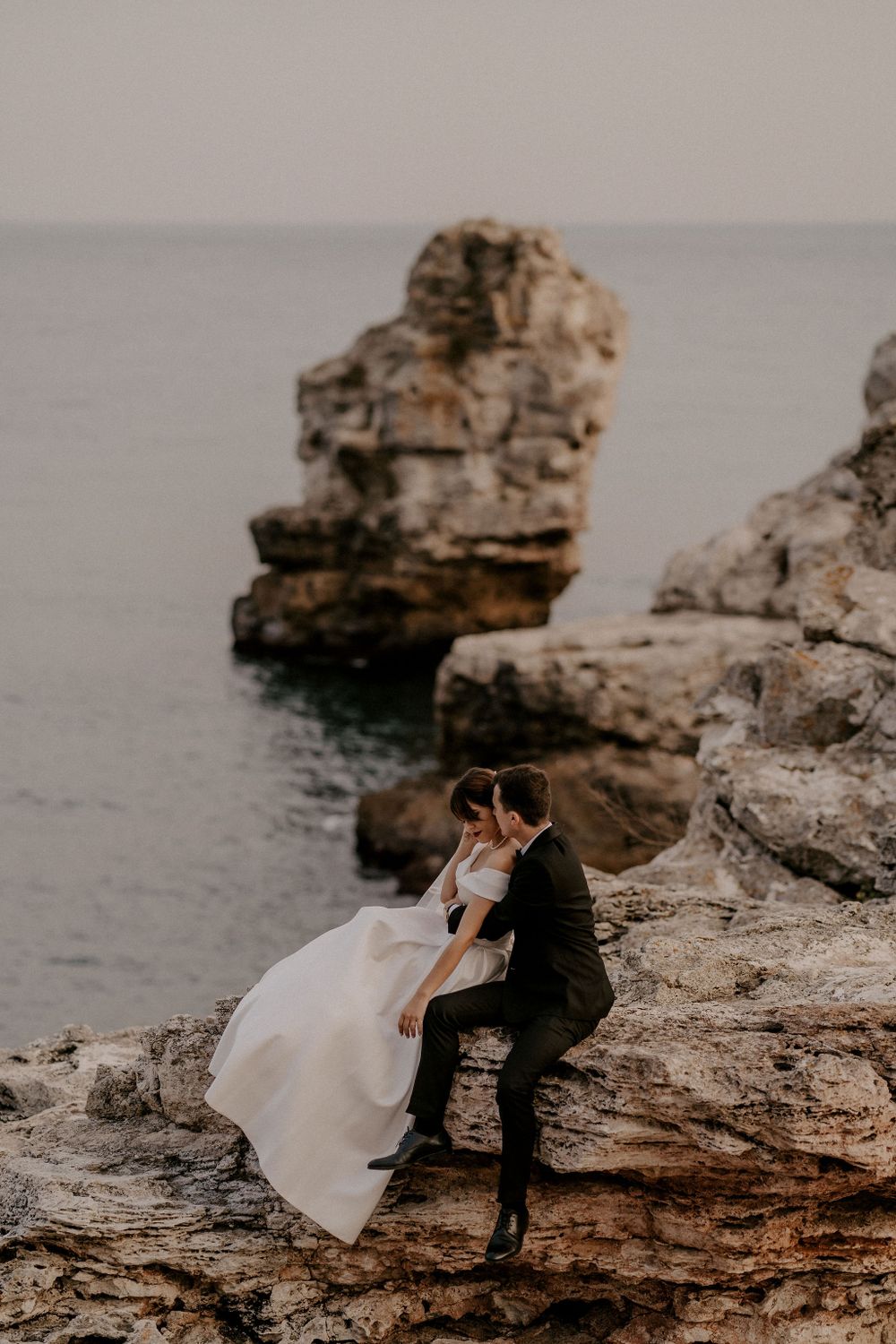 Dramatic wedding portrait on rocky coastal ledge with ocean vista.