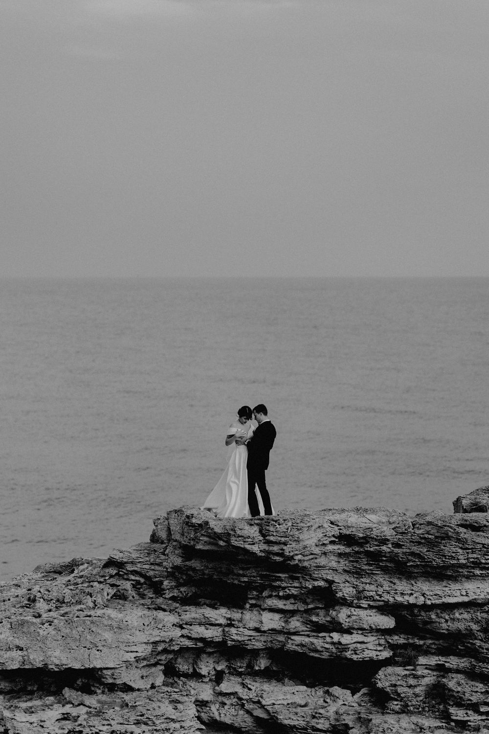 Silhouetted figures stand on dramatic coastal cliffs against a misty ocean horizon.