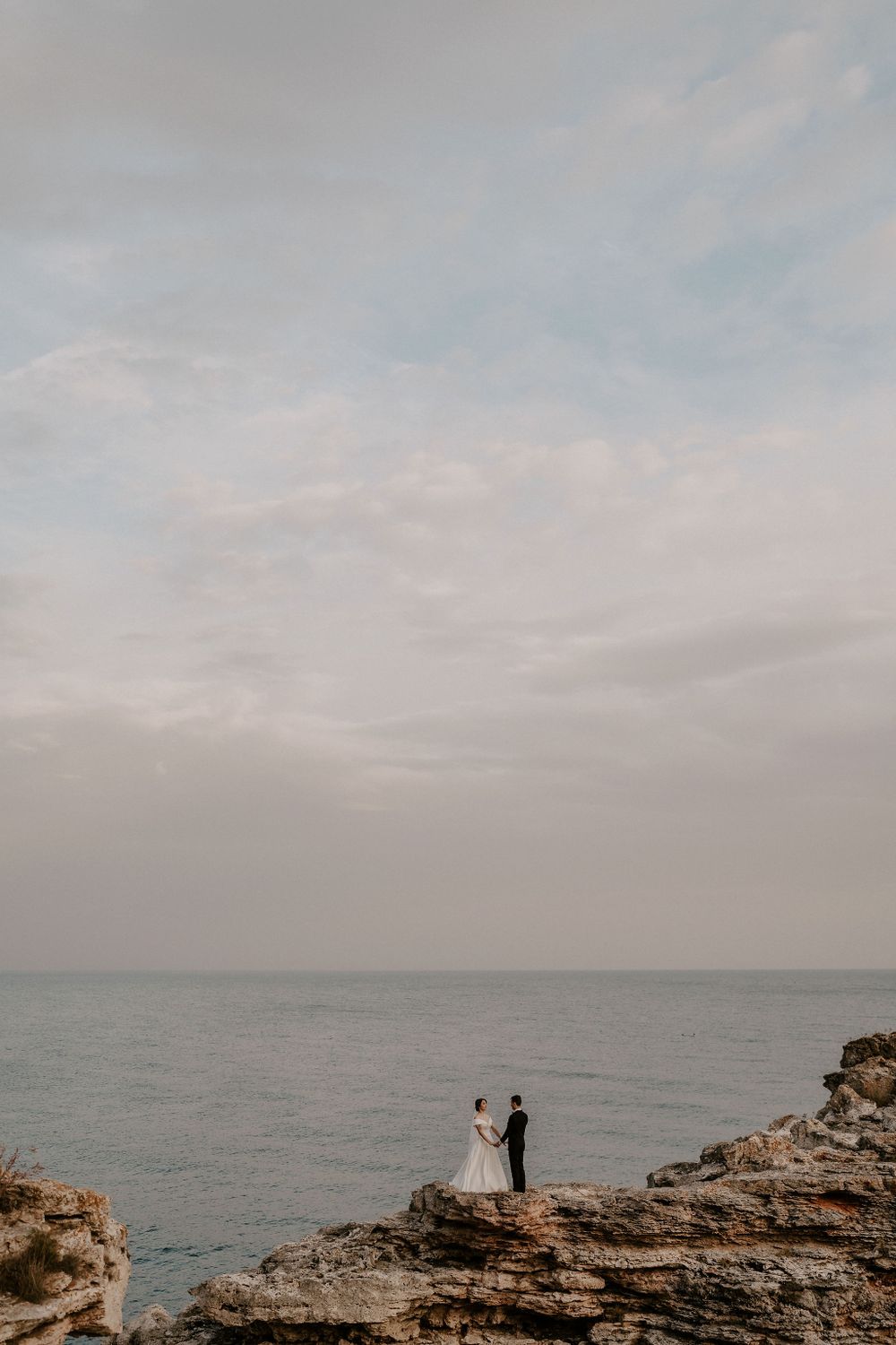 Two figures stand on dramatic coastal cliffs against an overcast ocean backdrop.