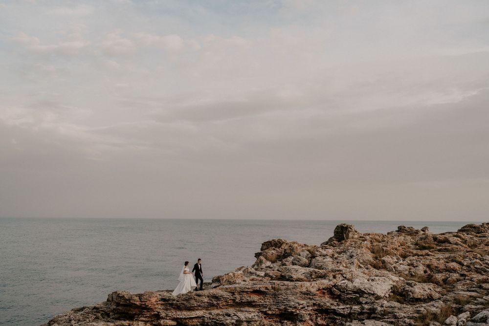 Distant figures stand on rocky coastal cliffs under cloudy skies.