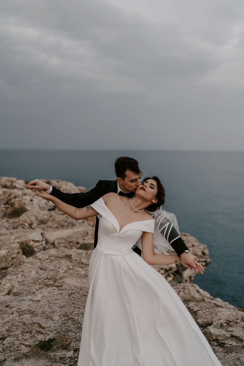A romantic wedding photoshoot on dramatic seaside cliffs with overcast skies.