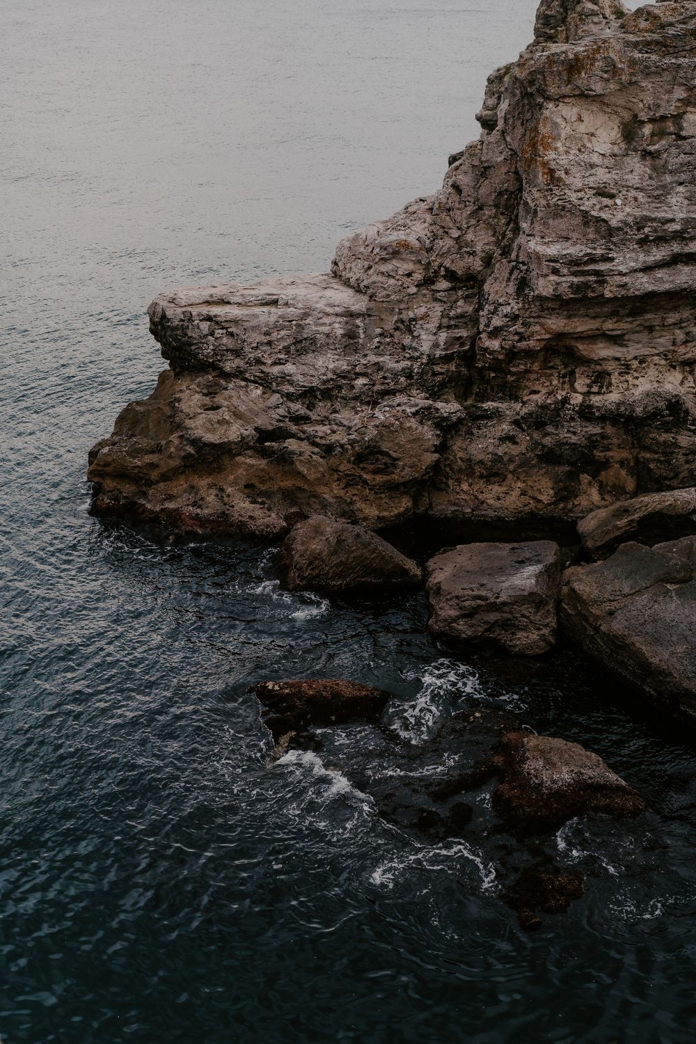 Waves crash against rocky coastal cliffs with deep blue ocean waters below.