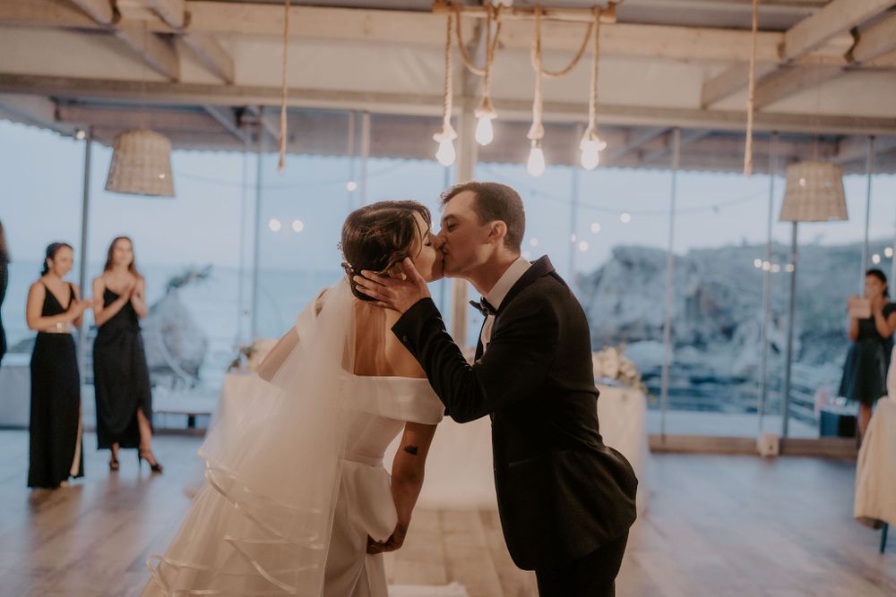 A couple shares their first dance in an industrial-style venue with hanging lights and white decor.