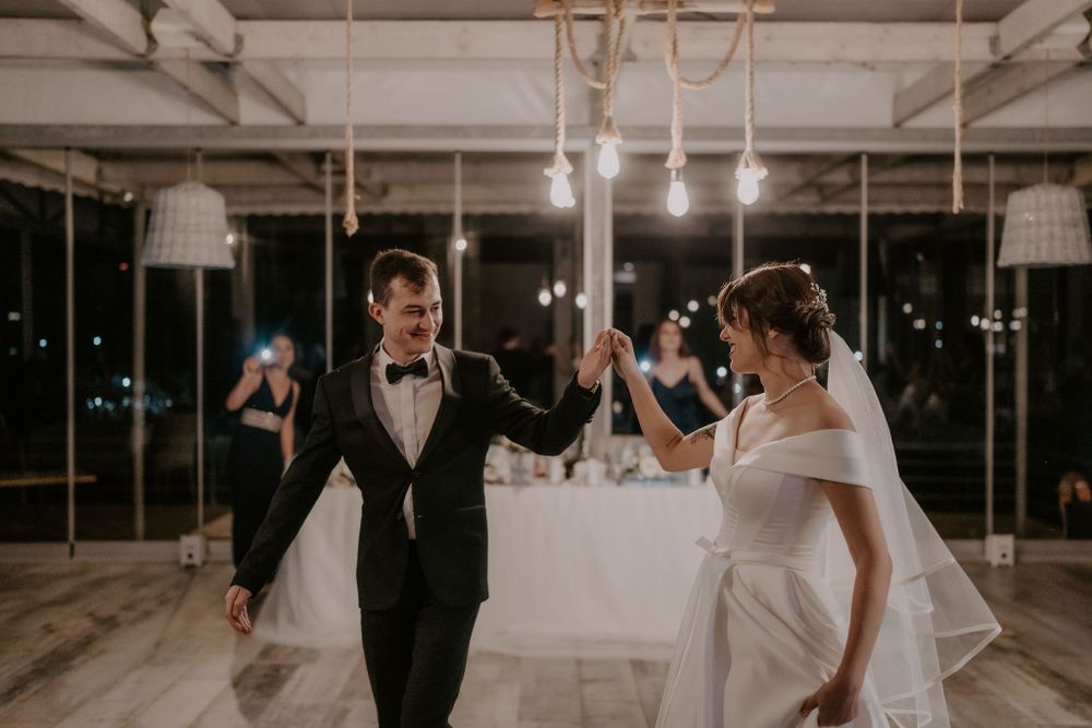A romantic first dance moment captured in an industrial venue with exposed beams and string lights.