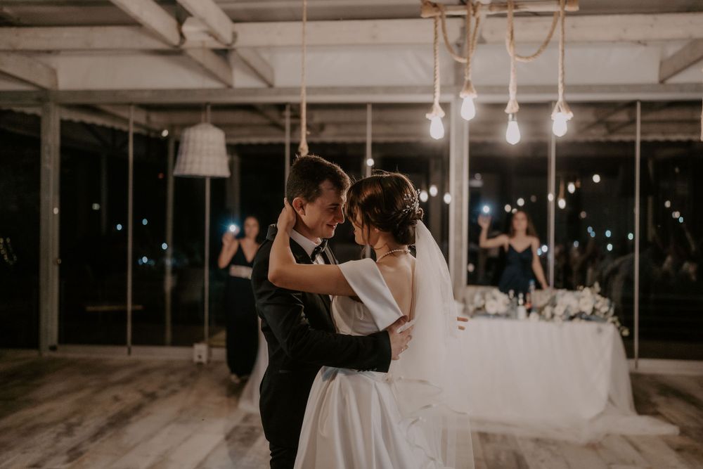 A couple dances together in an elegant white reception space with modern lighting fixtures.