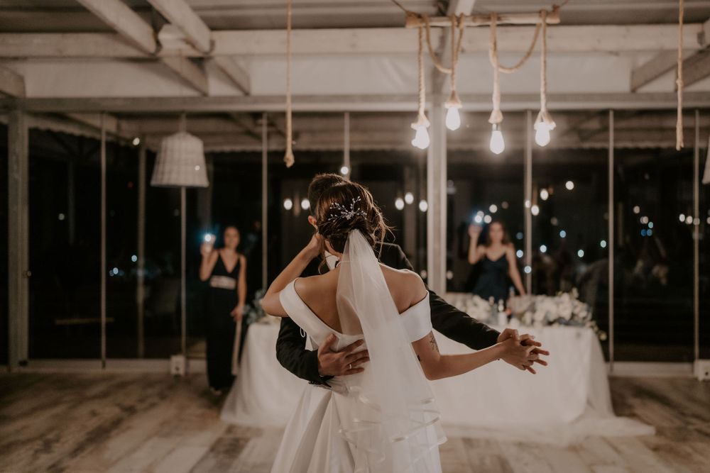 A tender moment during a wedding dance in a rustic-modern venue with ambient lighting.