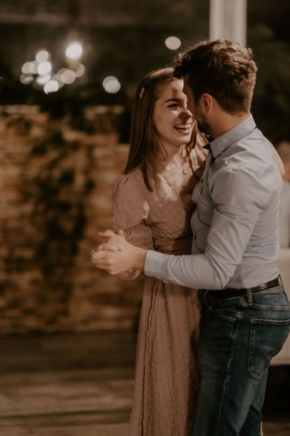 Couple sharing a joyful dance moment in casual attire with romantic lighting.
