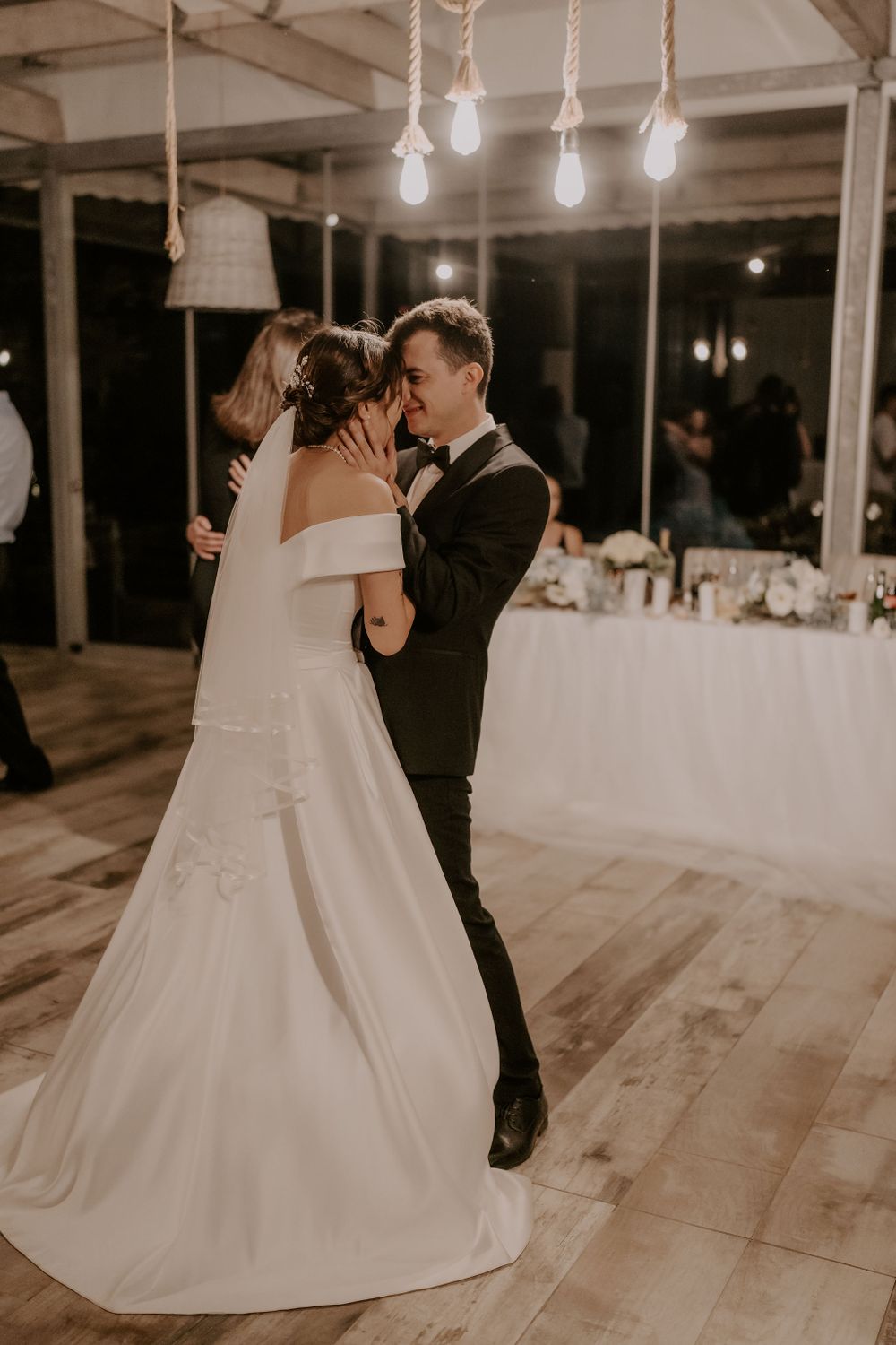 Elegant first dance moment in a reception venue with hanging Edison bulbs and wooden floors.