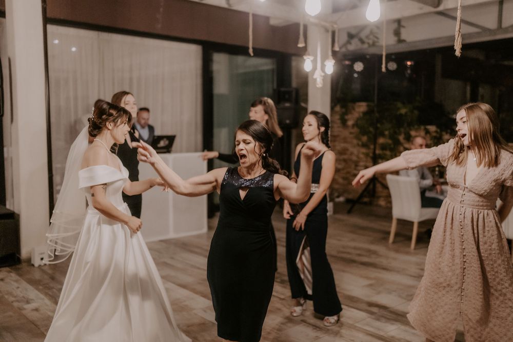 Wedding party dancing and celebrating in an elegant indoor venue with hanging lights.