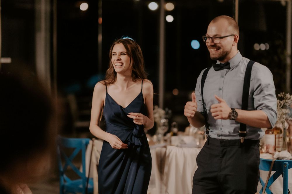 Guests at a wedding reception share a joyful moment during speeches, with elegant lighting in the background.
