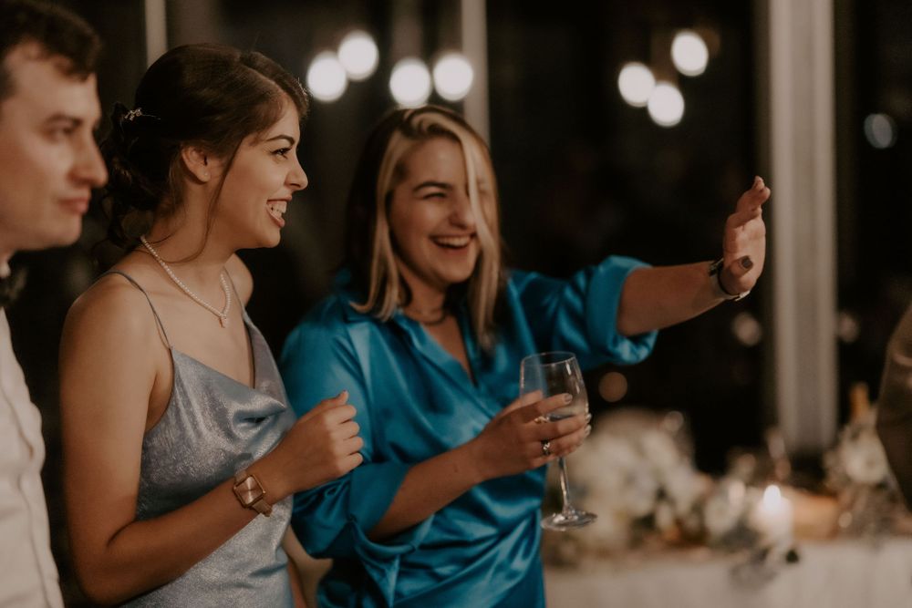 Wedding guests laugh and celebrate together during an evening reception with bokeh lights.