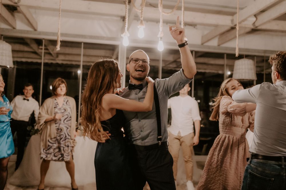 Wedding guests dance energetically on the reception dance floor under pendant lights.