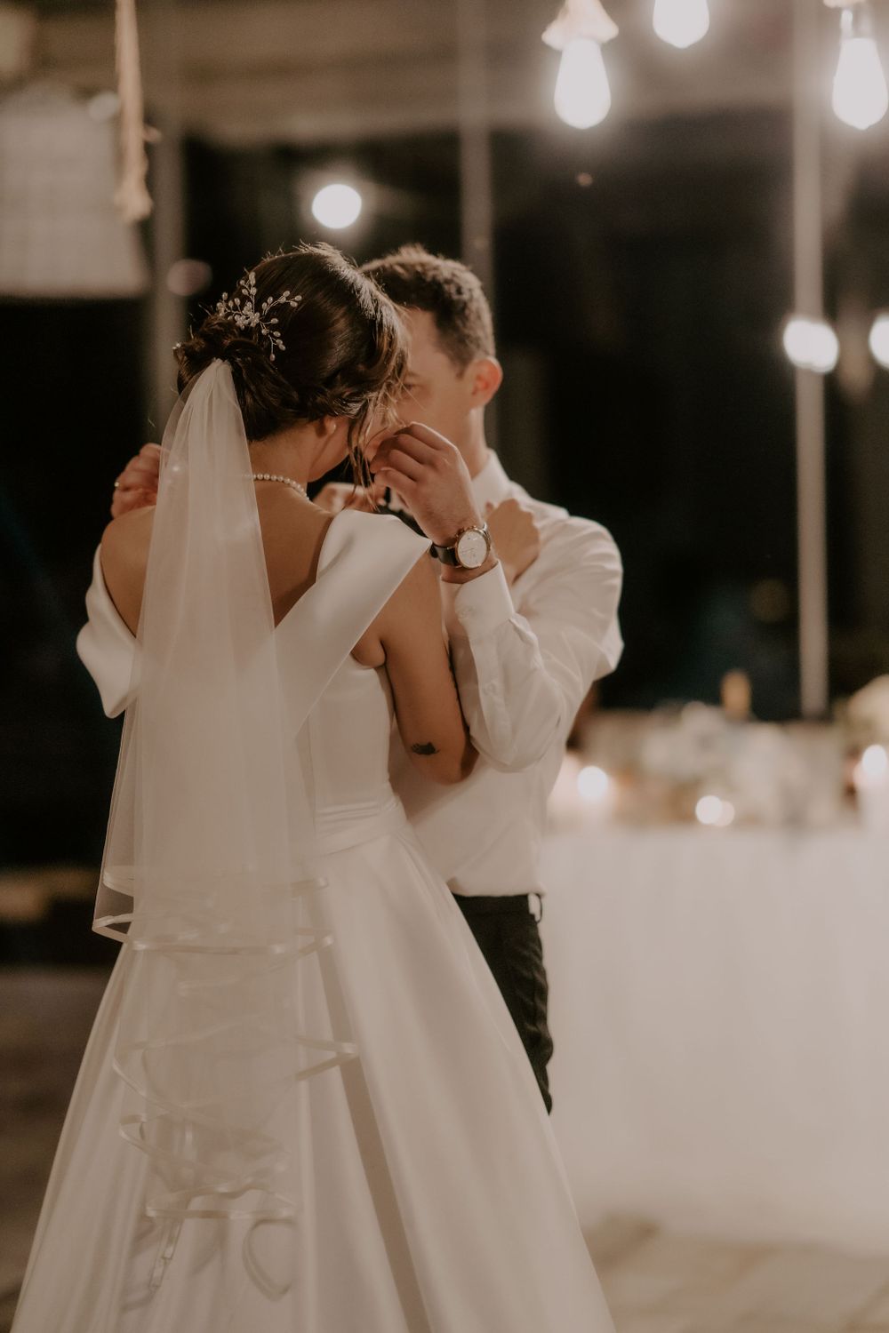 Romantic dance moment captured at dimly lit wedding reception with string lights overhead.