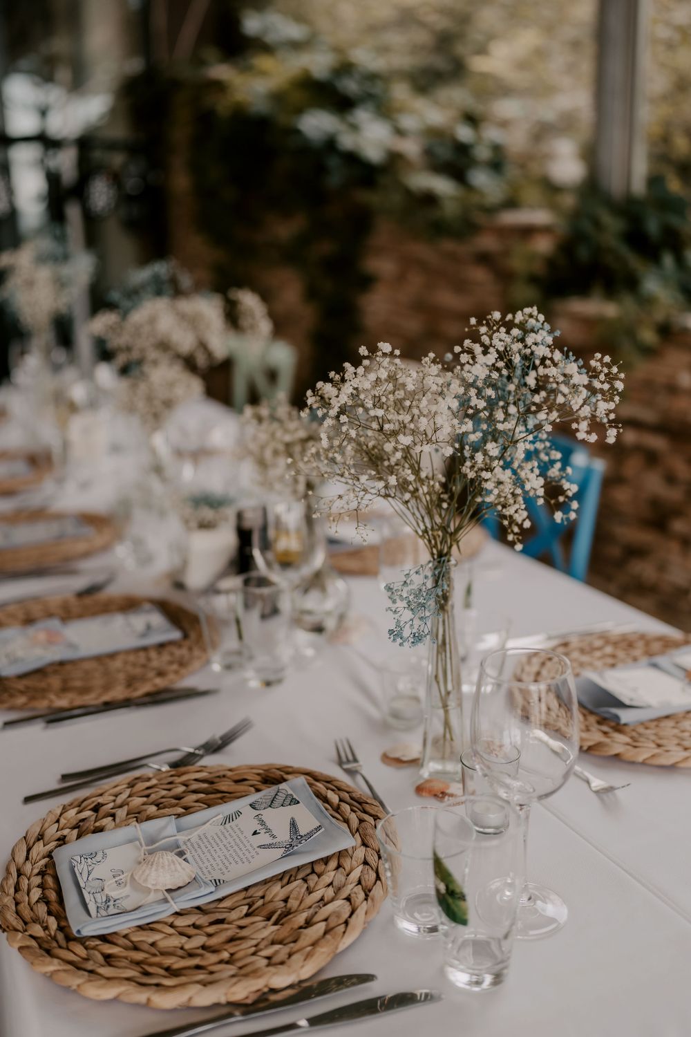 Elegant wedding table setting with baby's breath centerpieces and woven placemats on white linens.