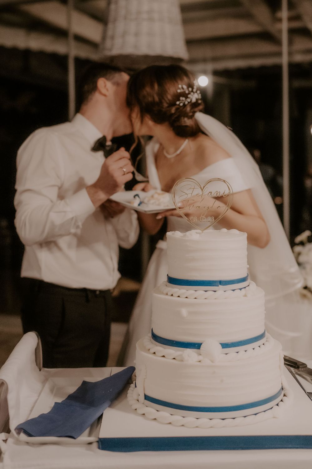 Traditional white wedding cake with blue ribbon trim being shared by newlyweds.