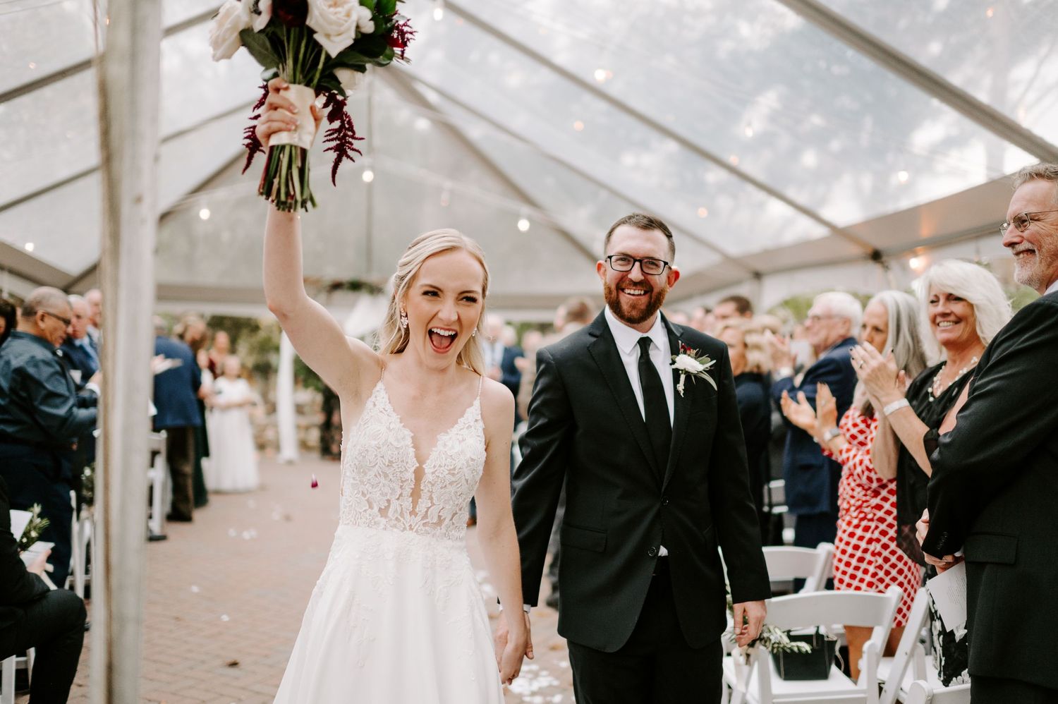 Wedding celebration under clear tent with guests watching happy couple.