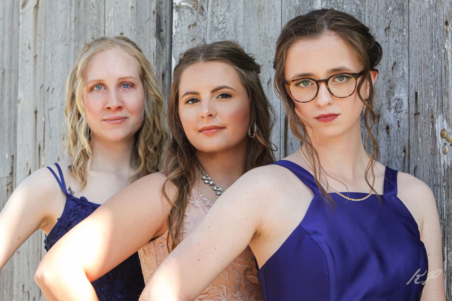 Group photo showing several people wearing blue and formal attire standing against a weathered wooden wall.