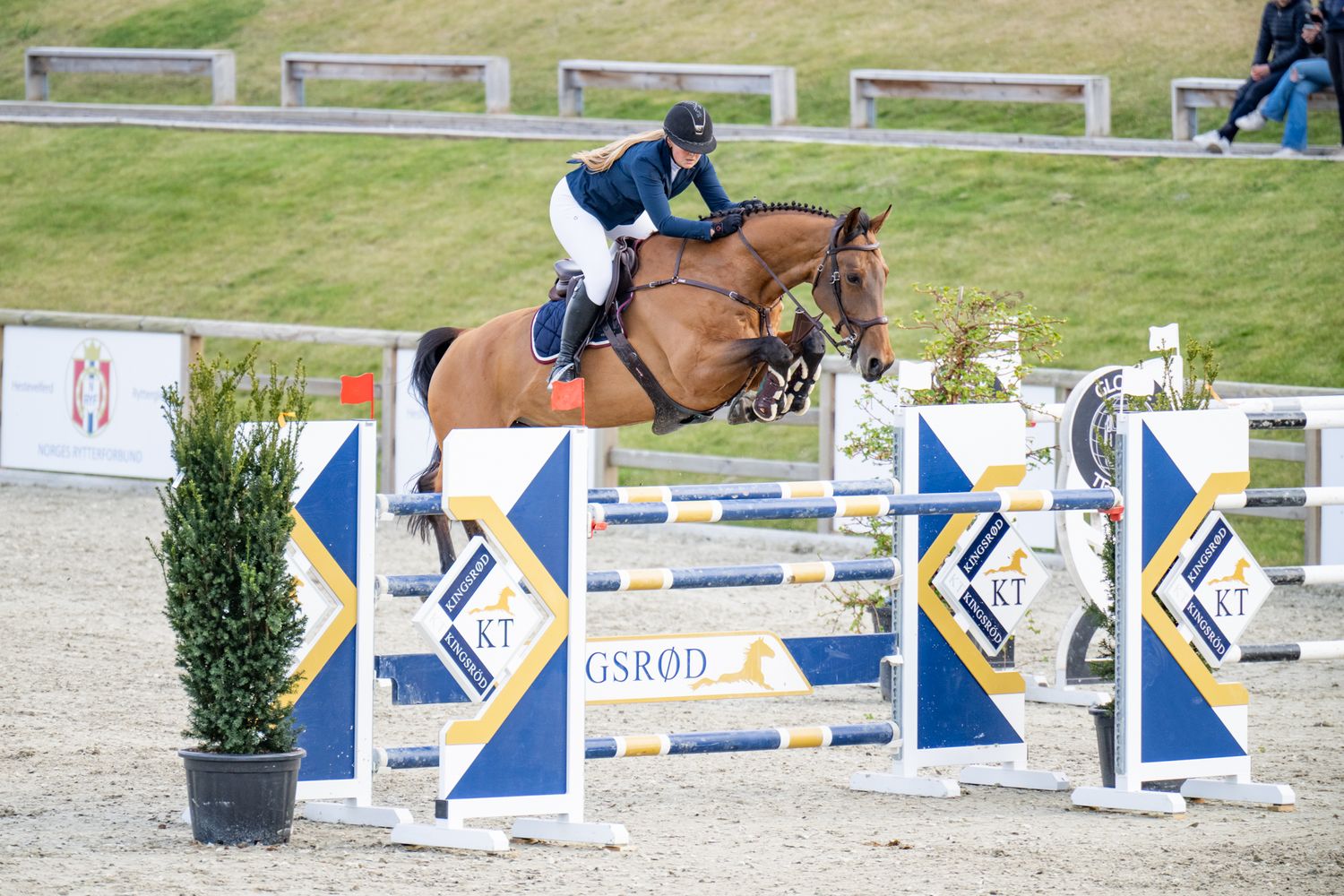 Horse and rider jumping over blue and white competition obstacle in outdoor arena.