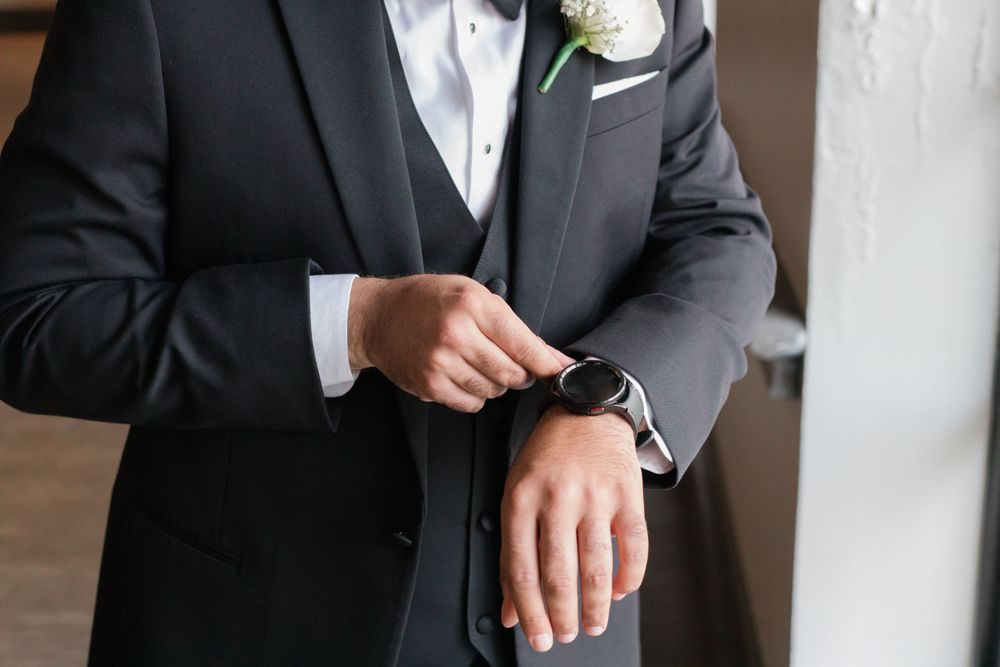 Detail shot of a groom checking his watch while wearing a classic black tuxedo.