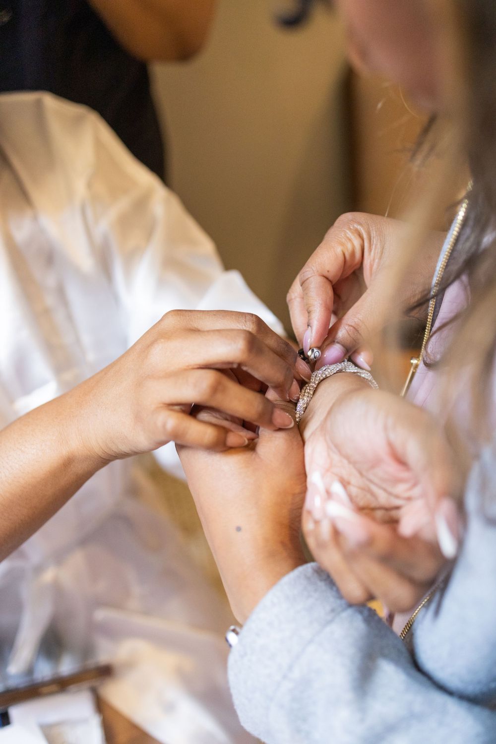 Hands in white satin robe adjusting delicate jewelry.