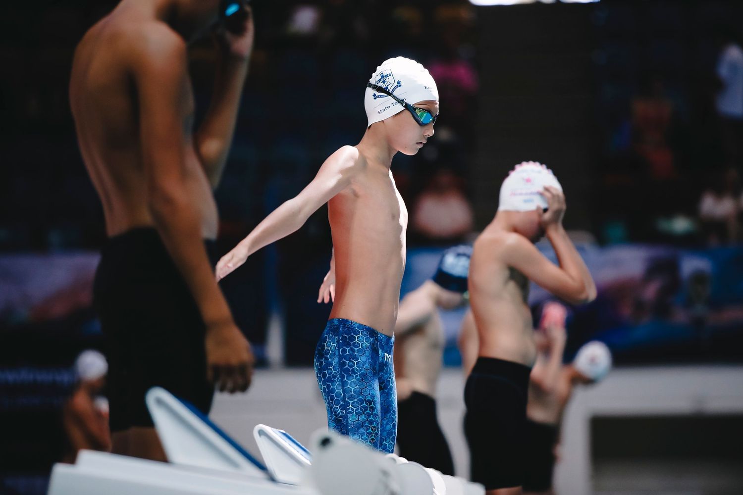 Young swimmers lined up on starting blocks preparing for race.
