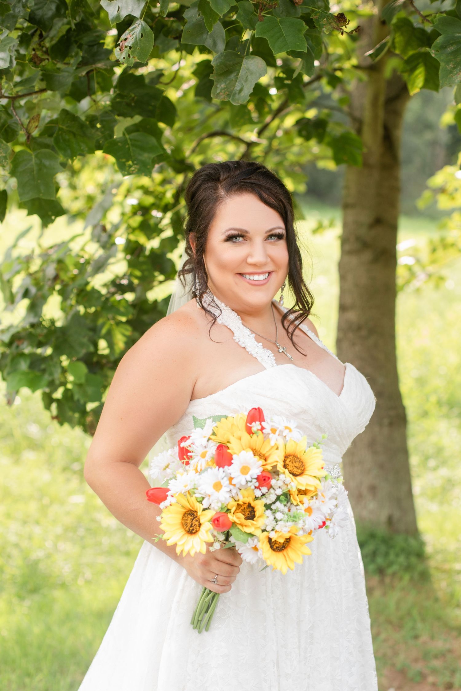 Bride holding vibrant sunflower and daisy bouquet in outdoor garden setting.