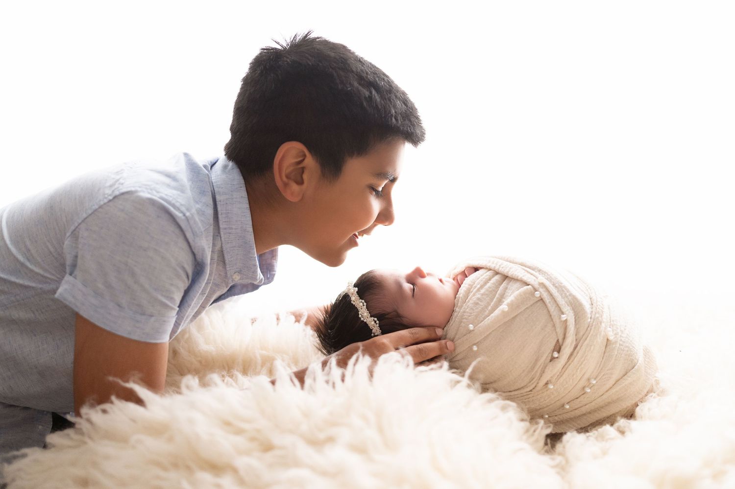 Family members leaning in close together during newborn photo session on white backdrop.