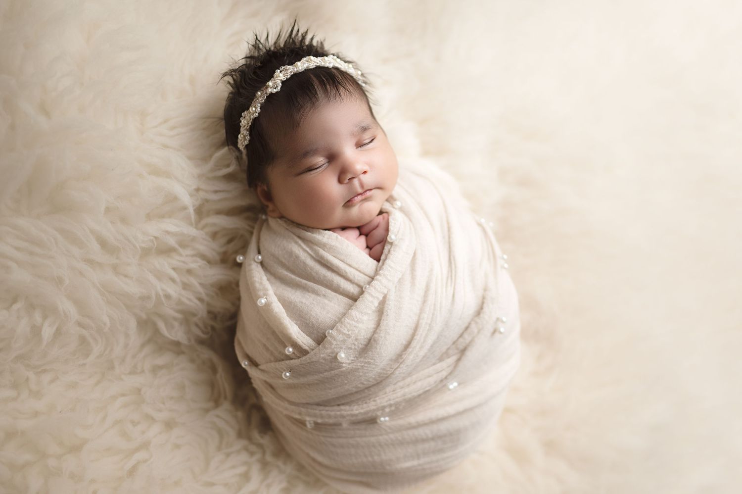 Newborn baby sleeping peacefully wrapped in cream colored swaddle.